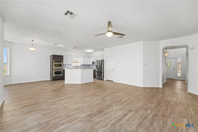 unfurnished living room with light wood-style floors, visible vents, a ceiling fan, and a wealth of natural light