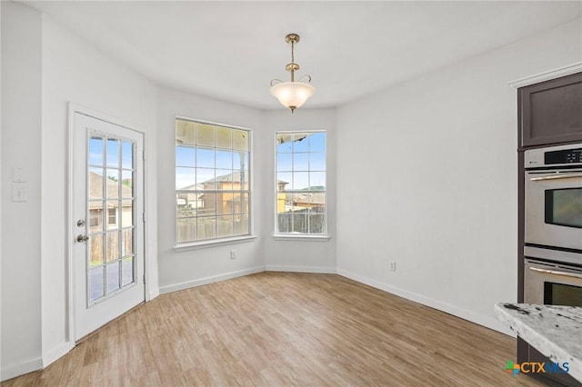 unfurnished dining area with light wood-type flooring and baseboards
