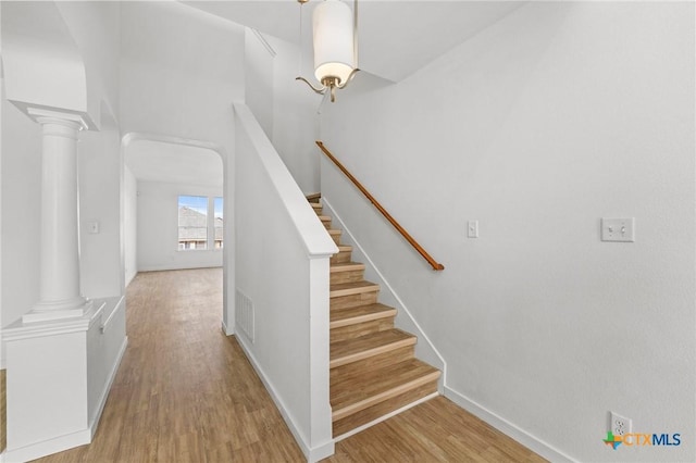 staircase with visible vents, baseboards, decorative columns, and wood finished floors