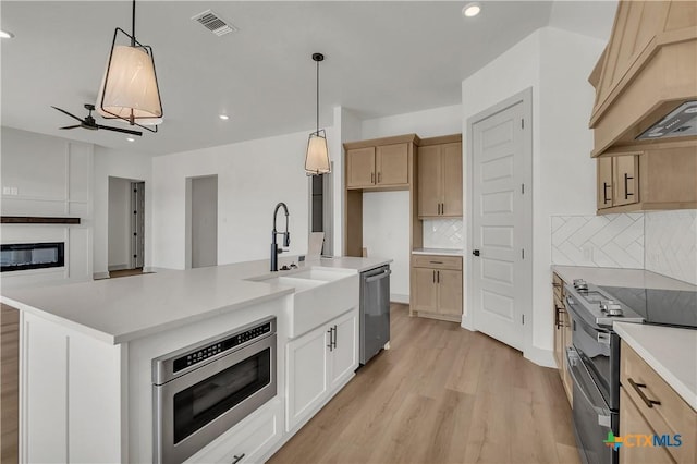 kitchen featuring custom exhaust hood, stainless steel appliances, an island with sink, decorative backsplash, and hanging light fixtures