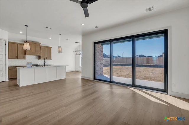 kitchen featuring tasteful backsplash, hanging light fixtures, light wood-type flooring, ceiling fan, and a center island with sink