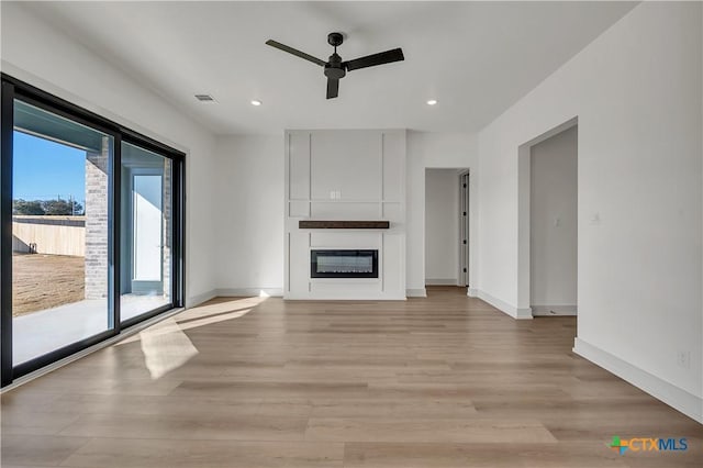 unfurnished living room with light hardwood / wood-style floors, a large fireplace, and ceiling fan