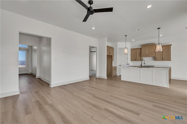 kitchen featuring light hardwood / wood-style floors, decorative backsplash, sink, decorative light fixtures, and a center island with sink