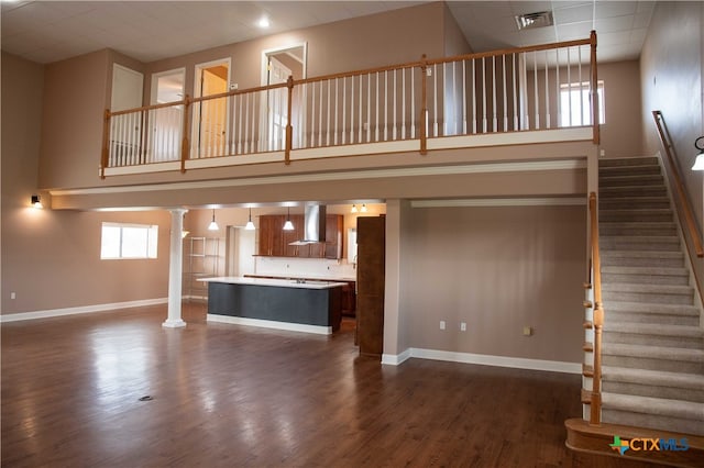 unfurnished living room featuring dark wood-type flooring, decorative columns, a towering ceiling, and baseboards