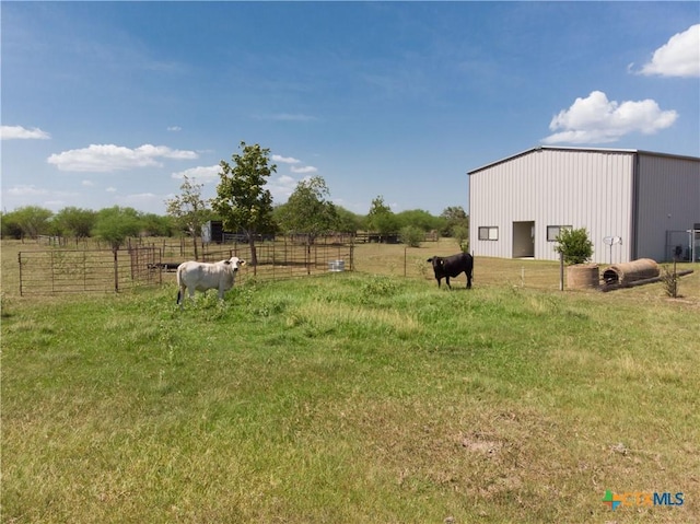 view of yard featuring a pole building, a rural view, an outdoor structure, and fence