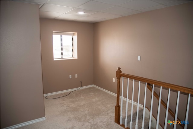 unfurnished room with light carpet, a drop ceiling, and baseboards