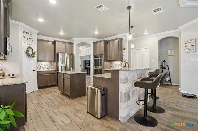 5106 La Piedra Ln, Killeen, TX 76549 - kitchen with arched walkways, appliances with stainless steel finishes, decorative backsplash, light wood-type flooring, and ornamental molding