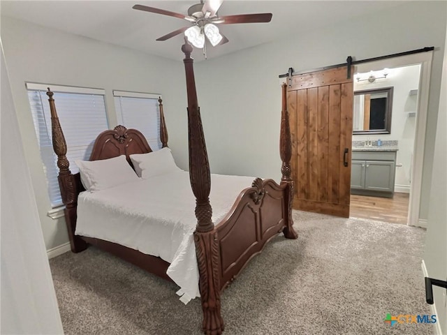 carpeted bedroom featuring a barn door, ensuite bathroom, sink, and ceiling fan