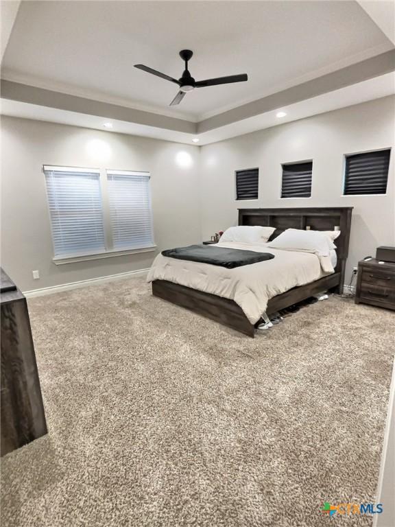 carpeted bedroom with a raised ceiling, ceiling fan, and ornamental molding