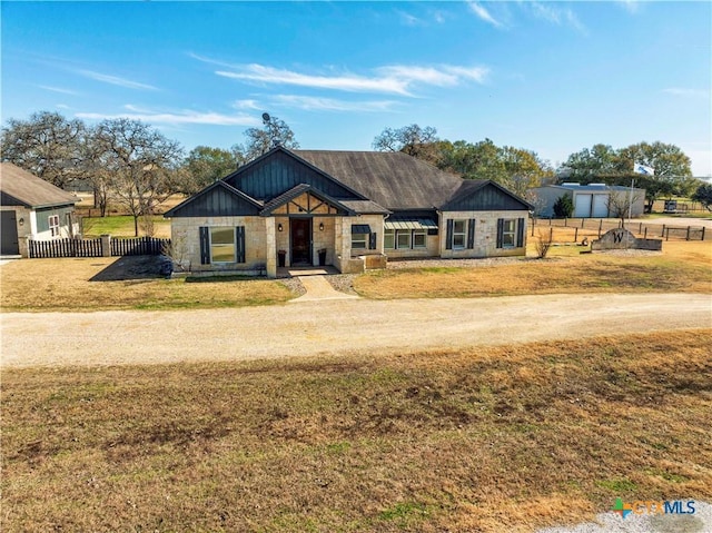 view of front of home featuring a front yard, fence, stone siding, and driveway