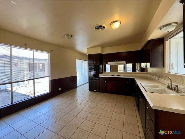 kitchen with visible vents, a wainscoted wall, a sink, black oven, and dark brown cabinets