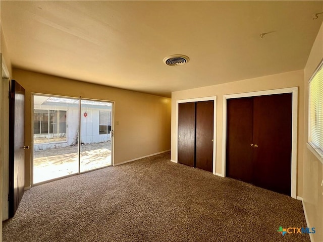 unfurnished bedroom with carpet, visible vents, and two closets