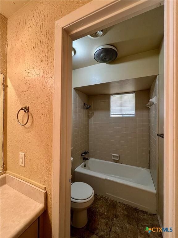 bathroom featuring vanity, washtub / shower combination, toilet, and a textured wall