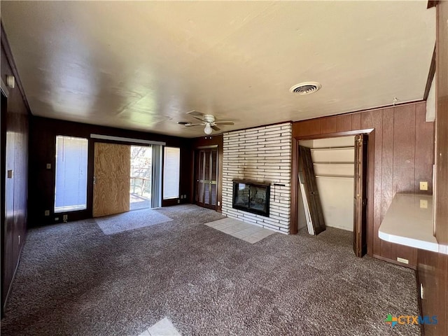 unfurnished living room with visible vents, carpet floors, a fireplace, ceiling fan, and wood walls