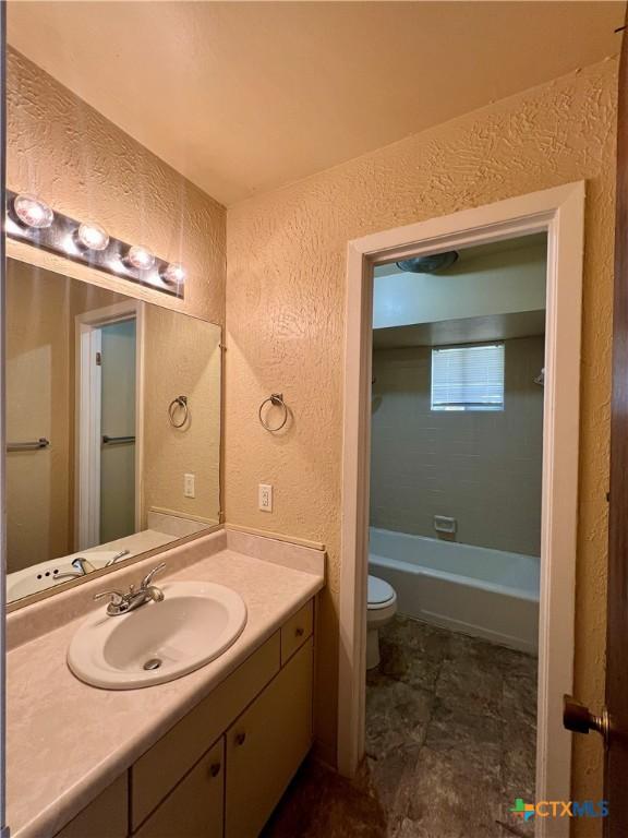 bathroom featuring a bath, toilet, vanity, and a textured wall