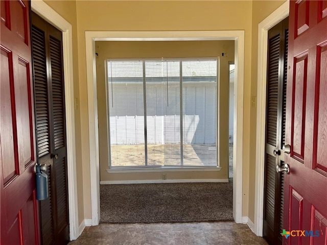 entrance foyer featuring baseboards and dark colored carpet