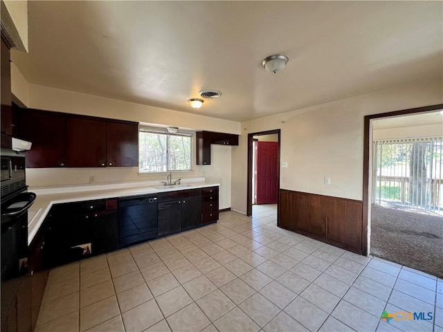 kitchen with dishwasher, light countertops, light tile patterned floors, wainscoting, and a sink