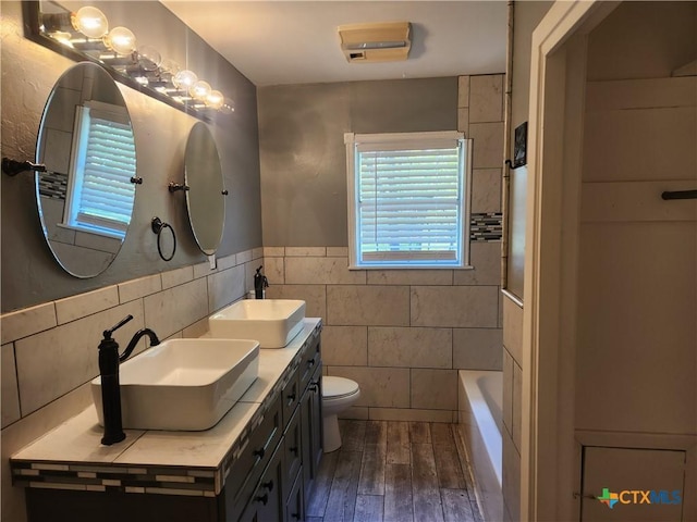 325 Montgomery St, Yoakum, TX 77995 - bathroom with tile walls, wood finished floors, double vanity, and a wainscoted wall