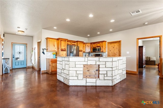 kitchen with a center island with sink, a textured ceiling, stainless steel appliances, and tasteful backsplash