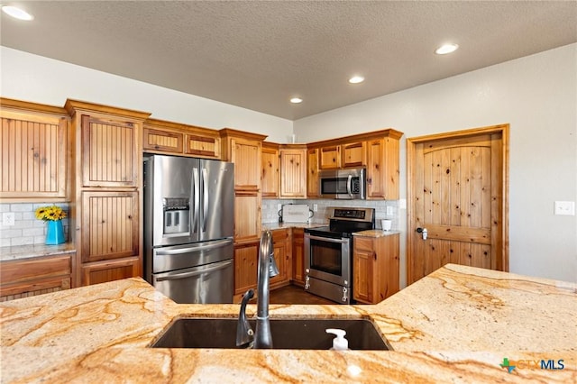 kitchen featuring tasteful backsplash, light stone countertops, sink, and appliances with stainless steel finishes