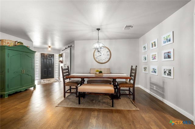 dining room with dark hardwood / wood-style flooring, a barn door, and a chandelier