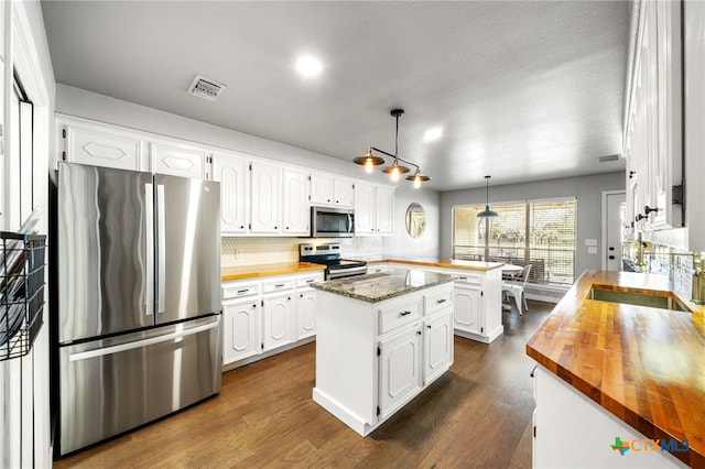 kitchen with appliances with stainless steel finishes, decorative light fixtures, dark stone countertops, white cabinets, and a center island