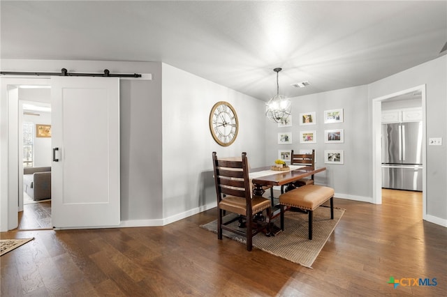 dining space with dark wood-type flooring, a barn door, and an inviting chandelier