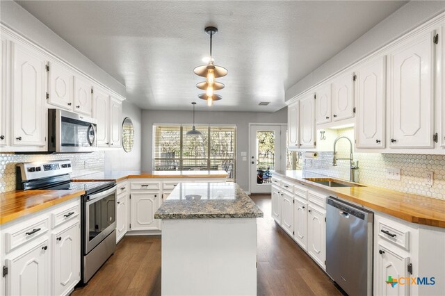 kitchen with sink, white cabinetry, hanging light fixtures, appliances with stainless steel finishes, and a kitchen island