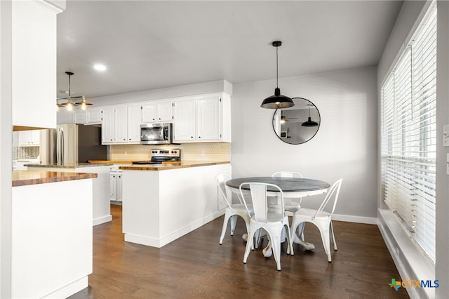 kitchen with pendant lighting, appliances with stainless steel finishes, white cabinets, wood counters, and kitchen peninsula