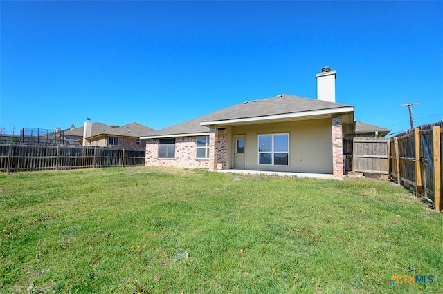 back of house with brick siding, a lawn, a chimney, and a fenced backyard