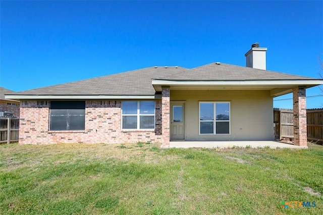 back of property with brick siding, fence, a lawn, a chimney, and a patio