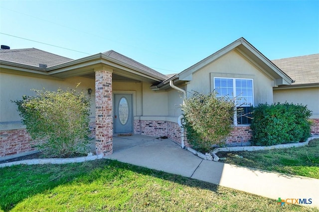 doorway to property featuring stucco siding, brick siding, and a shingled roof