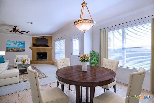 dining room featuring visible vents, a fireplace with raised hearth, ornamental molding, light tile patterned floors, and baseboards