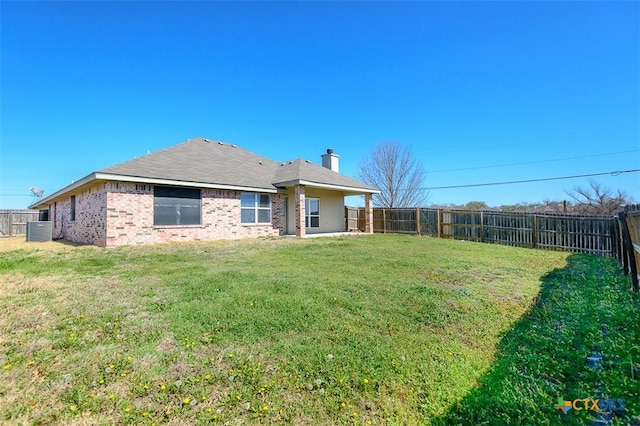 rear view of property featuring brick siding, central air condition unit, a lawn, a chimney, and a fenced backyard