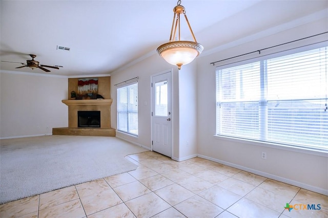 unfurnished living room with visible vents, a fireplace with raised hearth, light tile patterned flooring, crown molding, and light colored carpet