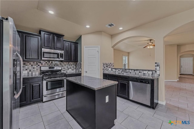 kitchen with stainless steel appliances, light stone countertops, a center island, and light tile patterned floors