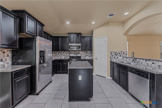 kitchen featuring light stone counters, stainless steel appliances, sink, and a kitchen island