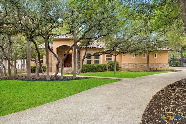 mediterranean / spanish-style home with stucco siding, stone siding, a front yard, and a tiled roof