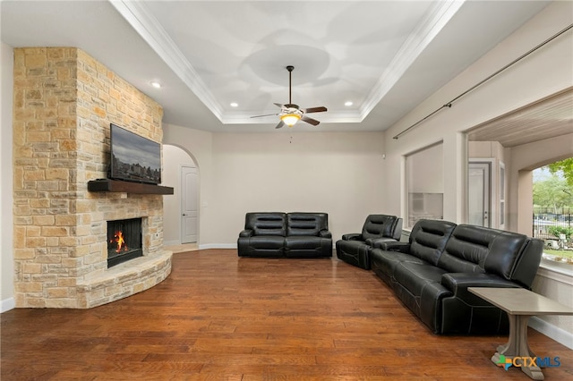 living room featuring a stone fireplace, hardwood / wood-style flooring, ceiling fan, crown molding, and a tray ceiling