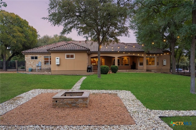 back of house at dusk featuring stucco siding, a tiled roof, a lawn, and an outdoor fire pit