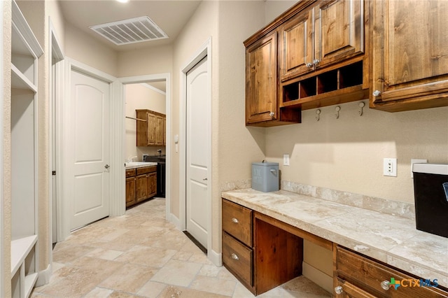 kitchen featuring visible vents, stone finish floor, open shelves, brown cabinetry, and built in study area