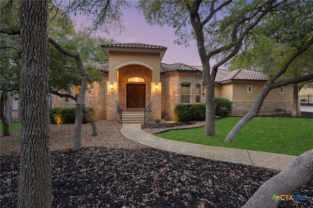 mediterranean / spanish house featuring a front yard, a tiled roof, stone siding, and stucco siding