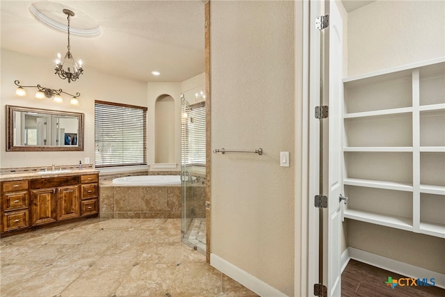 bathroom featuring vanity, baseboards, a stall shower, a garden tub, and a notable chandelier