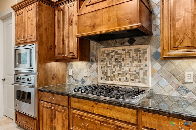 kitchen featuring custom exhaust hood, stainless steel appliances, dark stone counters, and tasteful backsplash