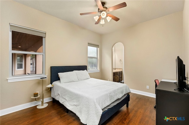 bedroom with dark wood-type flooring, arched walkways, baseboards, and connected bathroom