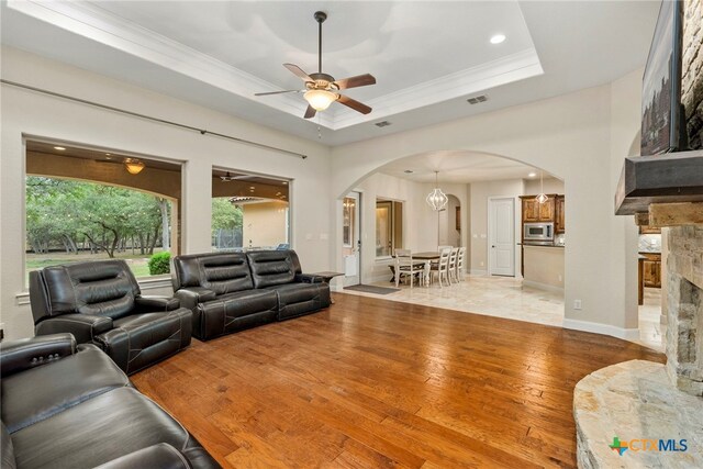 living room featuring a fireplace, wood-type flooring, ceiling fan, and a tray ceiling