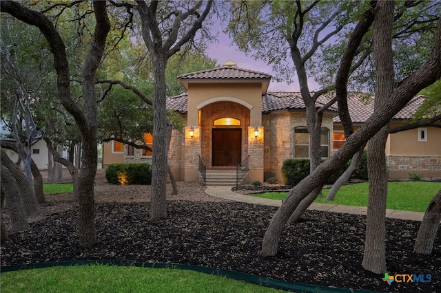 mediterranean / spanish-style house with a tile roof, stone siding, and stucco siding