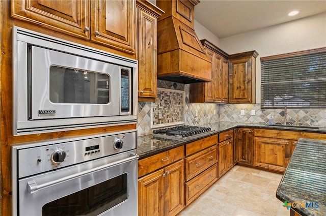 kitchen with stainless steel appliances, dark stone counters, sink, tasteful backsplash, and custom exhaust hood