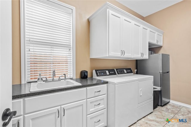 clothes washing area featuring separate washer and dryer, baseboards, cabinet space, and a sink