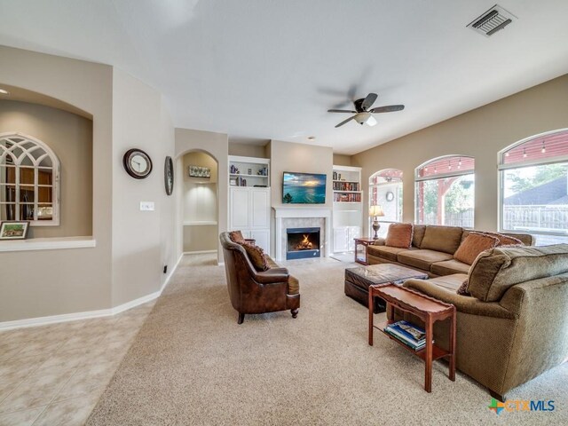 living area featuring a tile fireplace, built in shelves, baseboards, visible vents, and ceiling fan
